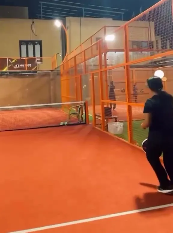 A player on the clay-red Club44 court at night, floodlights overhead