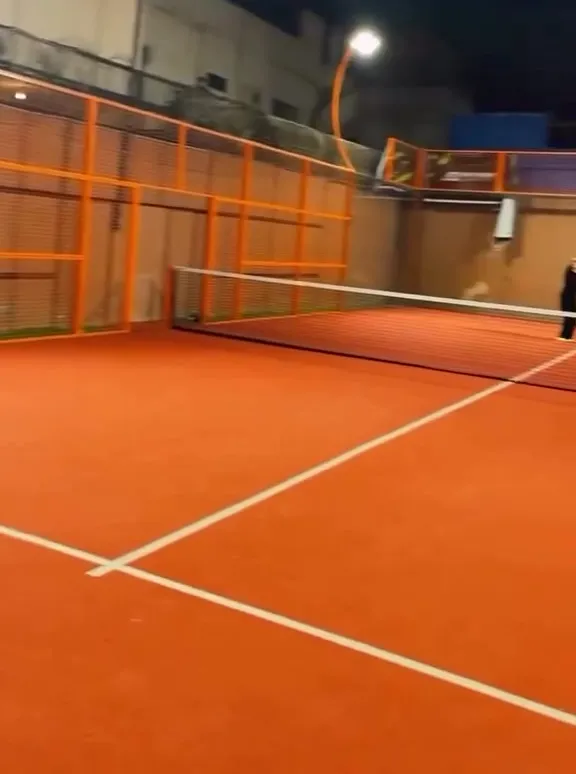 A Club44 padel court at night under floodlights, with its orange frame and net